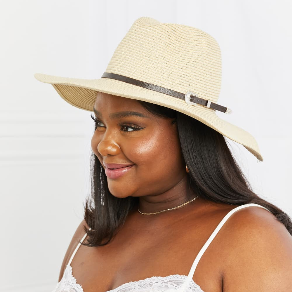 A woman wearing a beige straw fedora hat with a wide brim.